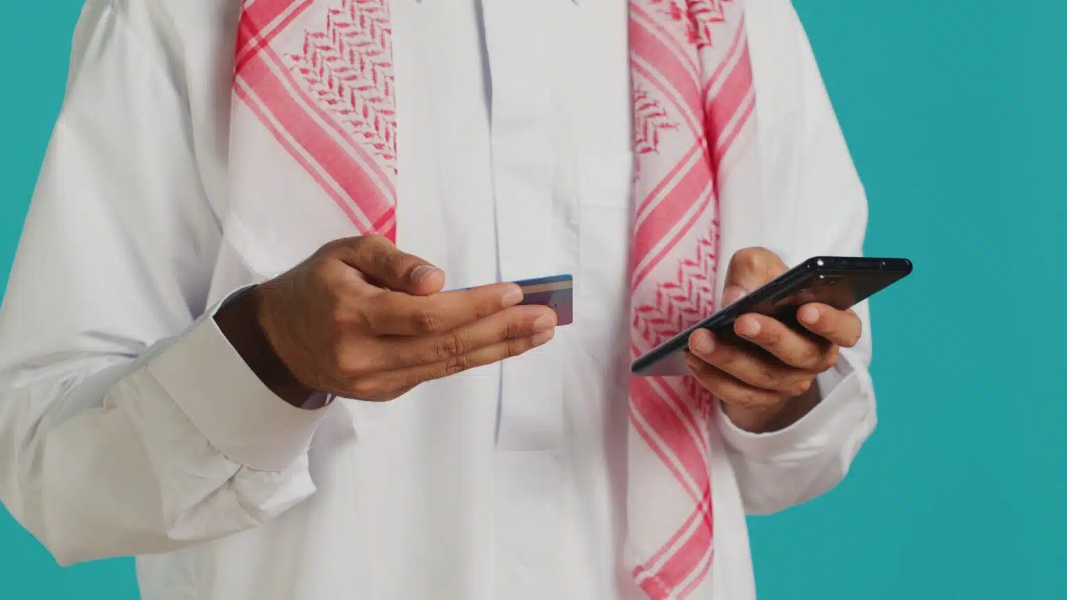 Man in traditional Gulf attire using a smartphone and credit card to pay GDRFA fines online.